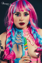 Load image into Gallery viewer, Person with vibrant pink and blue hair wearing a colorful outfit against a dark background
